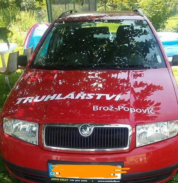 Obrázek červeného auta s polepem truhlářství na kapotě